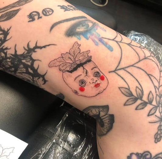 doll head tattoo with leaves growing from top